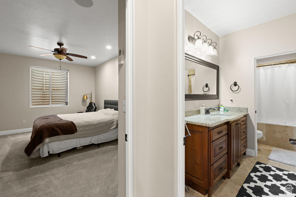 Bedroom featuring ceiling fan, ensuite bathroom, sink, and light carpet