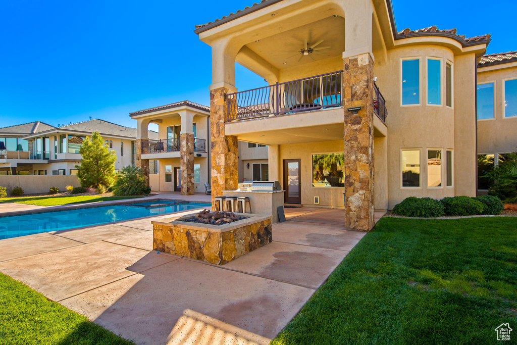 Rear view of property featuring a fenced in pool, ceiling fan, a yard, a balcony, and exterior kitchen