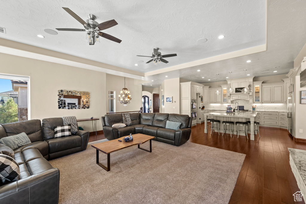 Living room with sink, dark hardwood / wood-style floors, a tray ceiling, a textured ceiling, and ceiling fan with notable chandelier