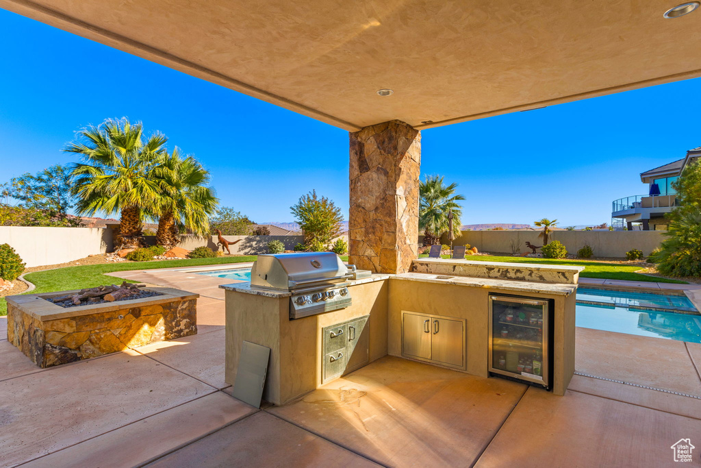 View of patio featuring wine cooler, grilling area, a fenced in pool, and exterior kitchen