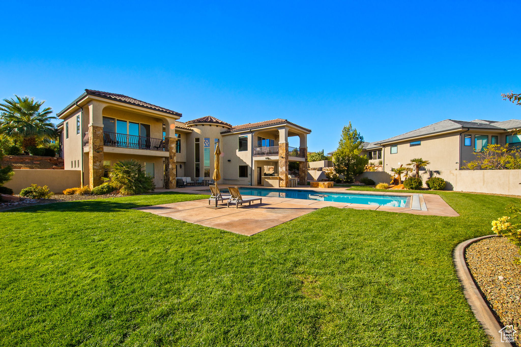 Rear view of property featuring a fenced in pool, a yard, a patio area, and a balcony