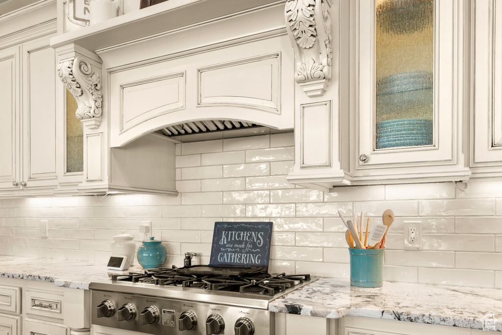 Kitchen featuring premium range hood, tasteful backsplash, stainless steel gas cooktop, light stone counters, and cream cabinets