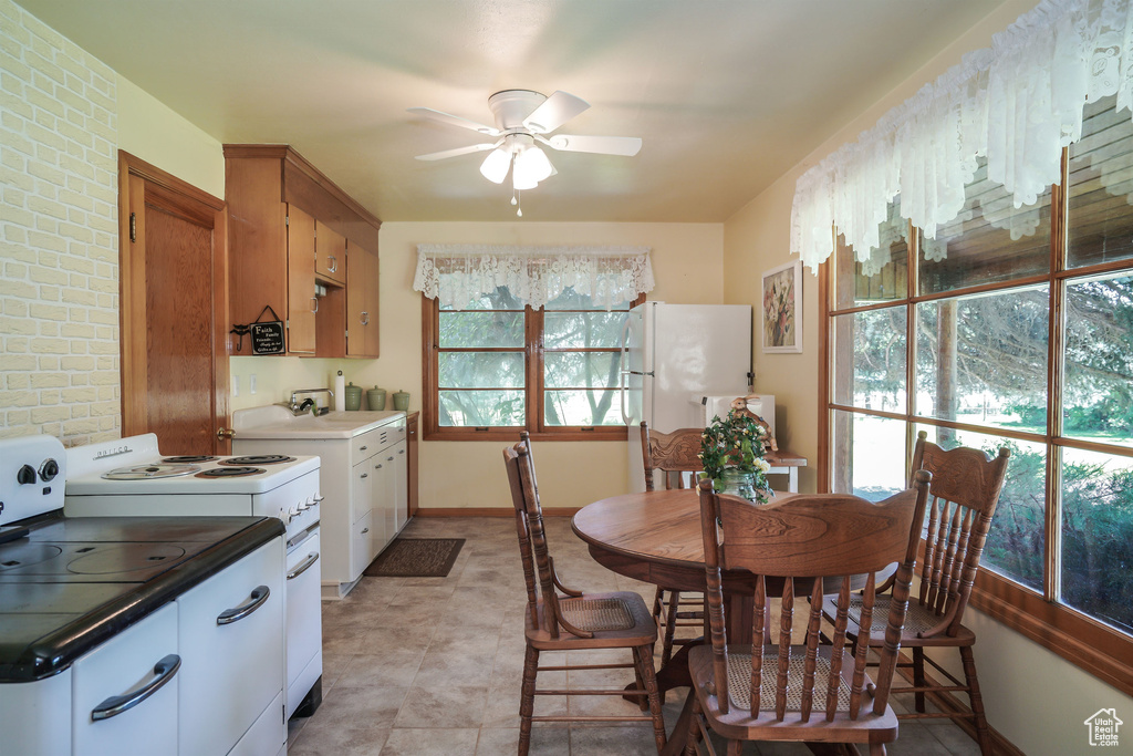 Kitchen with sink, white appliances, ceiling fan, brick wall, and light tile patterned flooring