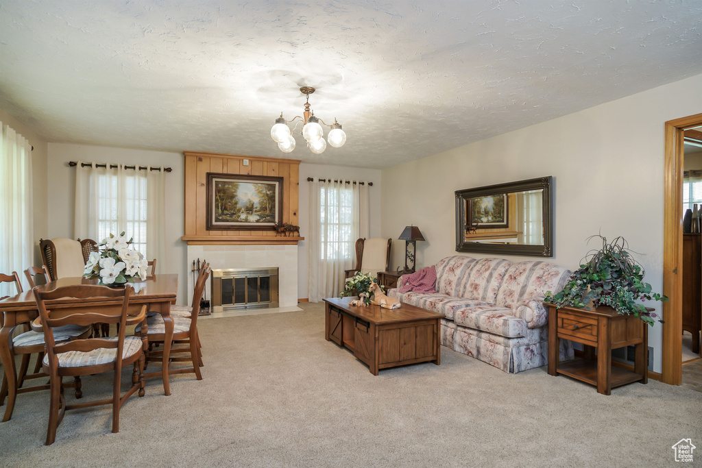 Carpeted living room featuring a tiled fireplace, a notable chandelier, and a textured ceiling