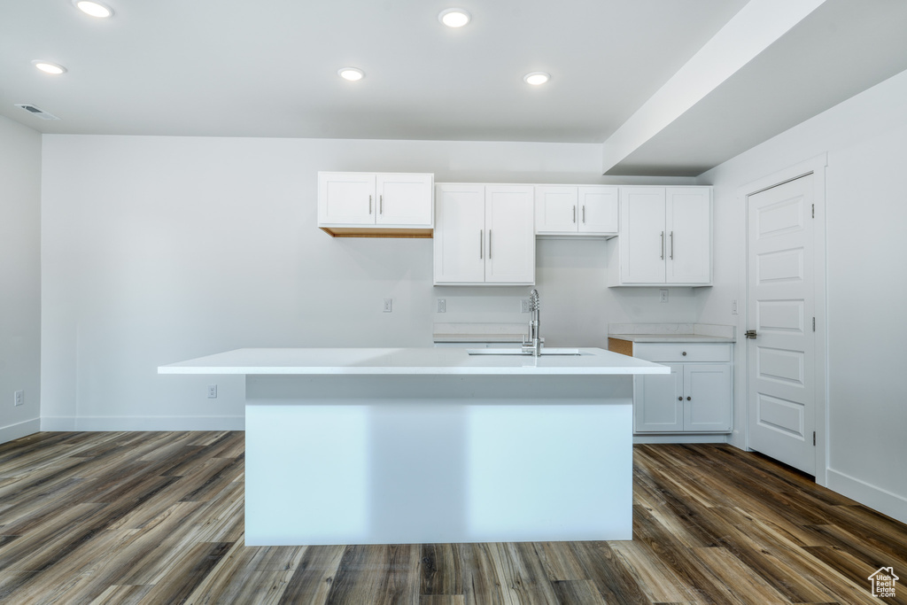 Kitchen with sink, dark hardwood / wood-style flooring, an island with sink, and white cabinets