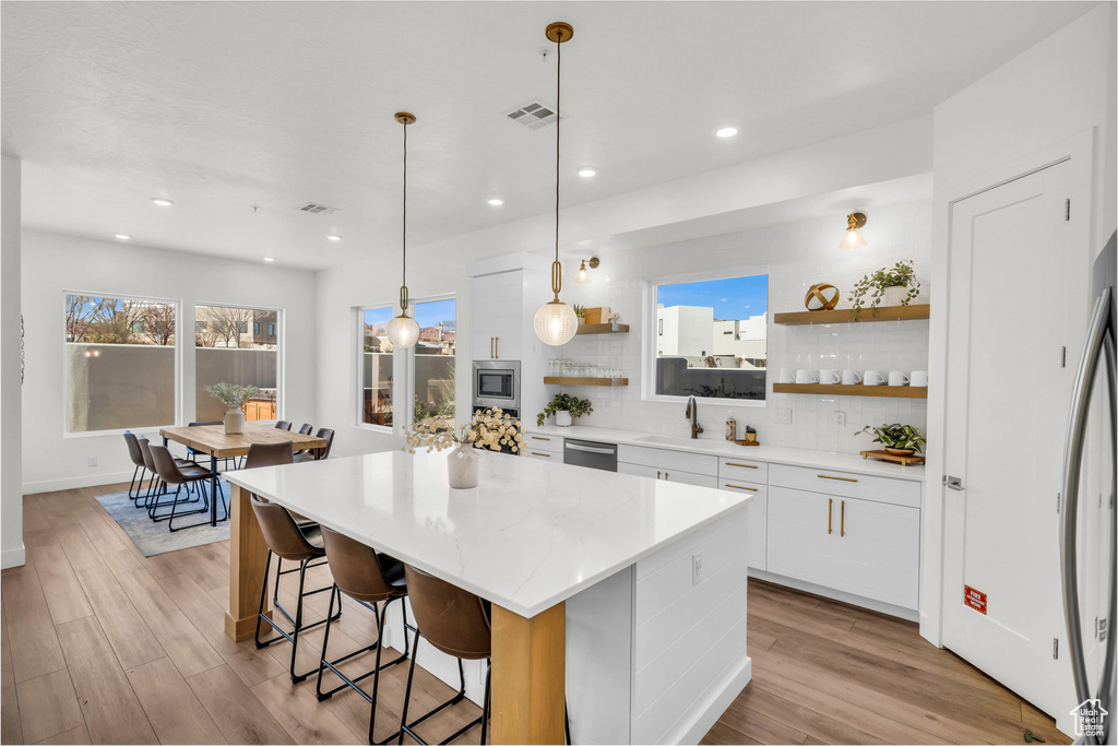 Kitchen with open shelves, a kitchen island, white cabinetry, backsplash, and a breakfast bar area