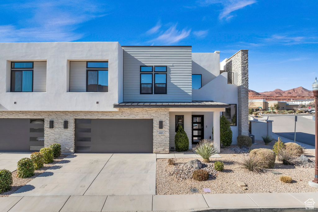 Contemporary home featuring a standing seam roof, concrete driveway, an attached garage, a metal roof, and stone siding