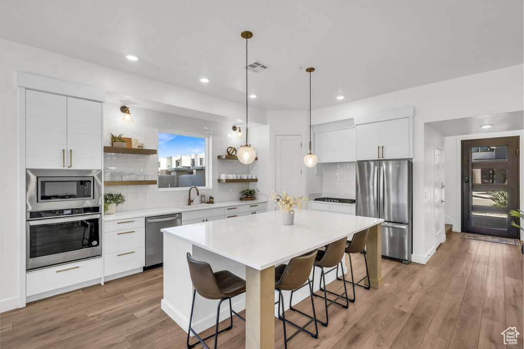 Kitchen with stainless steel appliances, open shelves, a kitchen breakfast bar, decorative backsplash, and recessed lighting