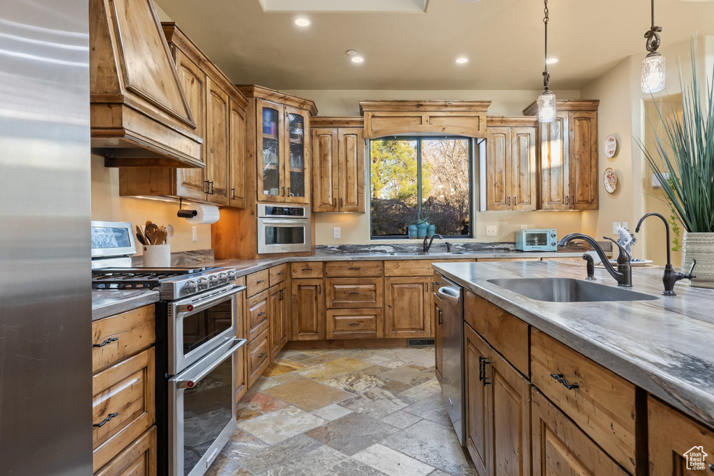 Kitchen with appliances with stainless steel finishes, premium range hood, a sink, stone tile floors, and recessed lighting