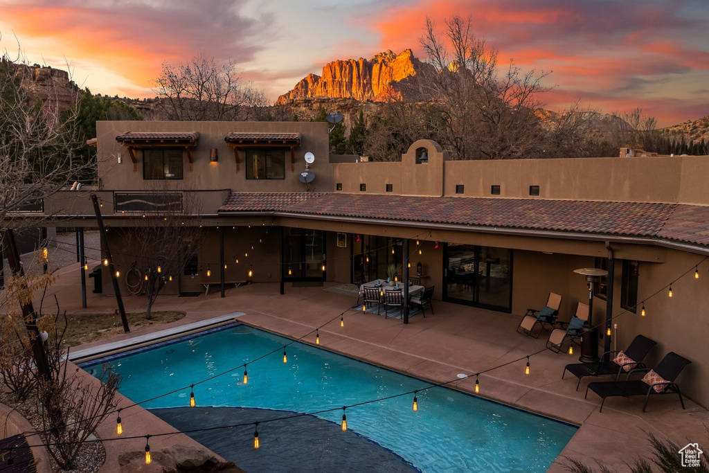 Back of house at dusk with a patio area, a tiled roof, and stucco siding