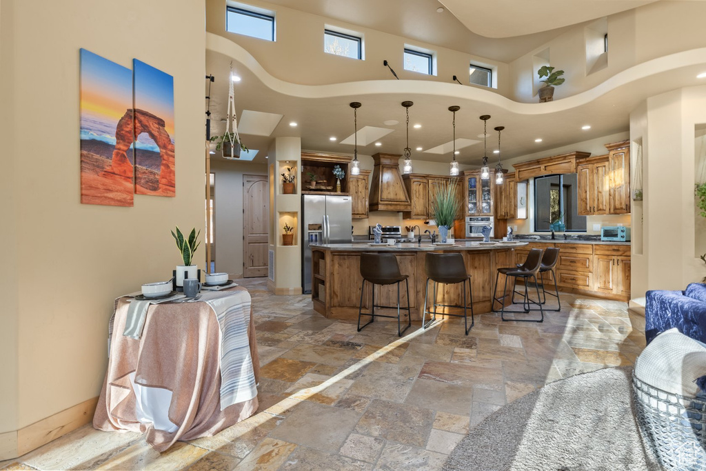 Kitchen featuring a high ceiling, appliances with stainless steel finishes, brown cabinets, a kitchen bar, and a large island