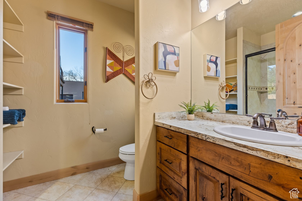 Bathroom featuring toilet, tile patterned floors, baseboards, vanity, and a shower with door