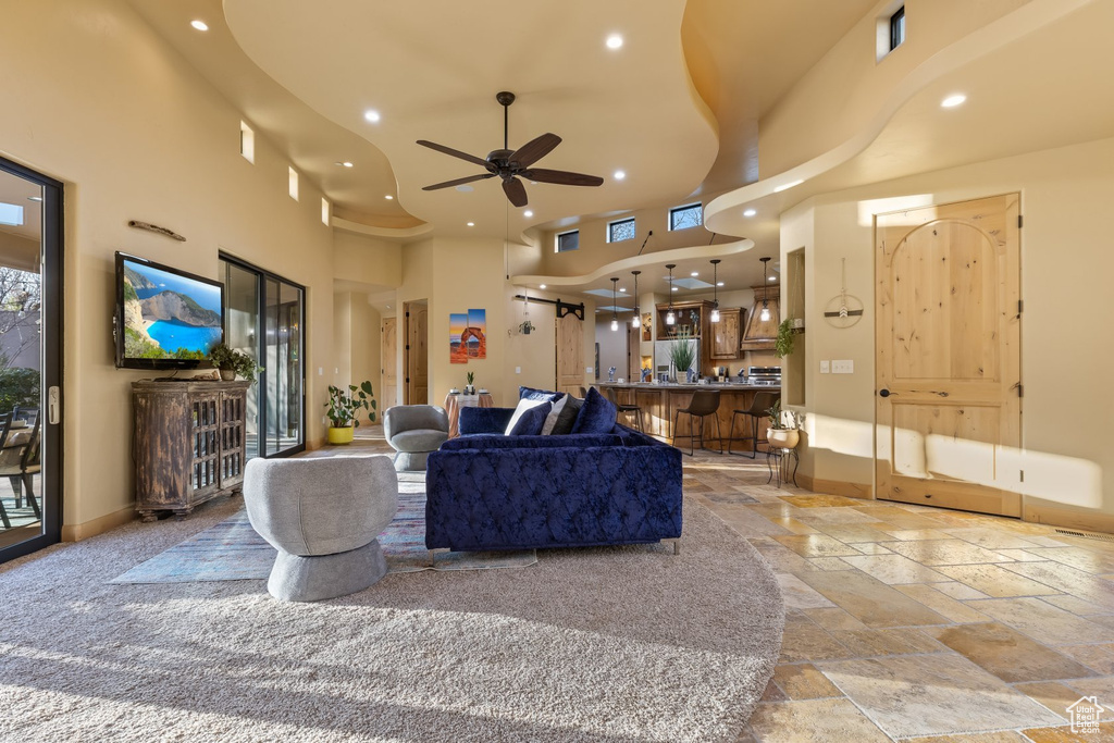 Living room featuring a towering ceiling, stone tile flooring, ceiling fan, recessed lighting, and baseboards