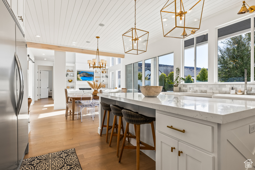 Kitchen featuring light stone counters, wood ceiling, a chandelier, built in fridge, and white cabinets