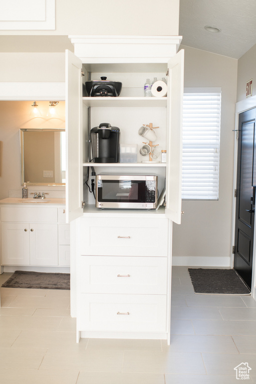 Kitchen with light tile patterned flooring, lofted ceiling, sink, and white cabinets