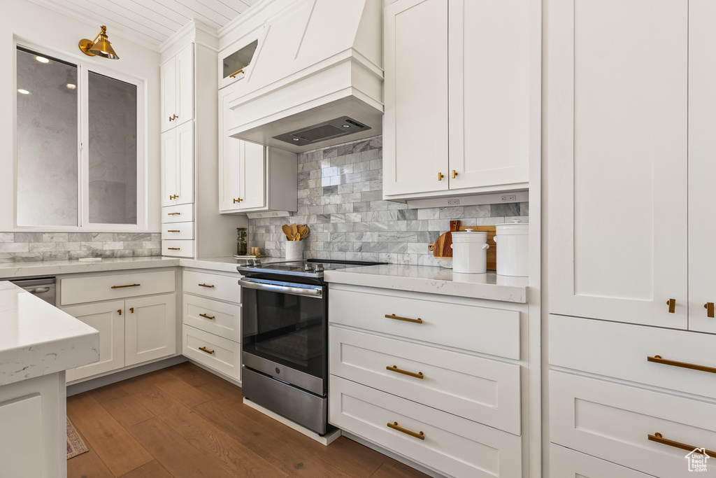 Kitchen featuring premium range hood, stainless steel range with electric stovetop, dark hardwood / wood-style floors, tasteful backsplash, and white cabinets