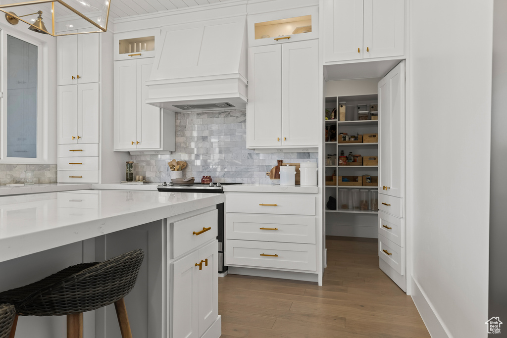 Kitchen with premium range hood, stainless steel electric range oven, white cabinetry, backsplash, and light wood-type flooring