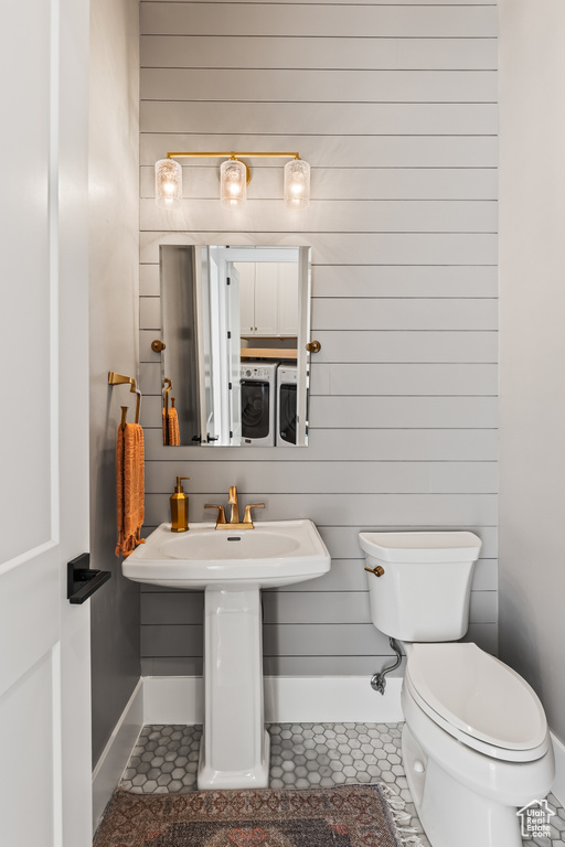 Bathroom with wooden walls, sink, tile patterned flooring, toilet, and washing machine and dryer