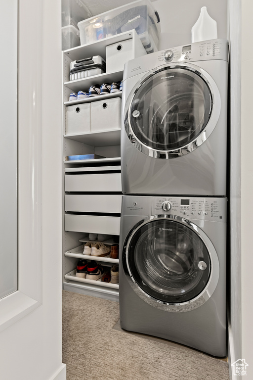 Laundry room featuring stacked washer and dryer and light colored carpet