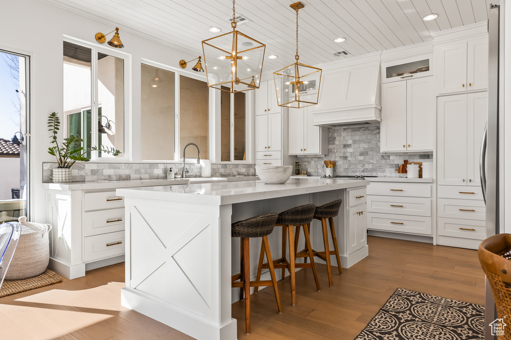 Kitchen with hanging light fixtures, premium range hood, white cabinets, and a kitchen island