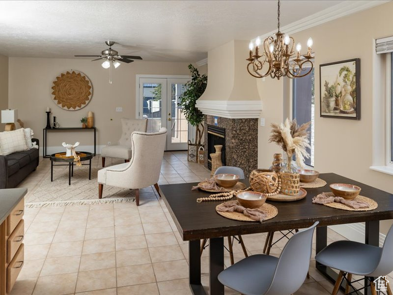Dining space with crown molding, a high end fireplace, light tile patterned flooring, ceiling fan with notable chandelier, and french doors