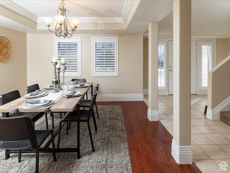 Dining space with a raised ceiling, crown molding, hardwood / wood-style flooring, and an inviting chandelier