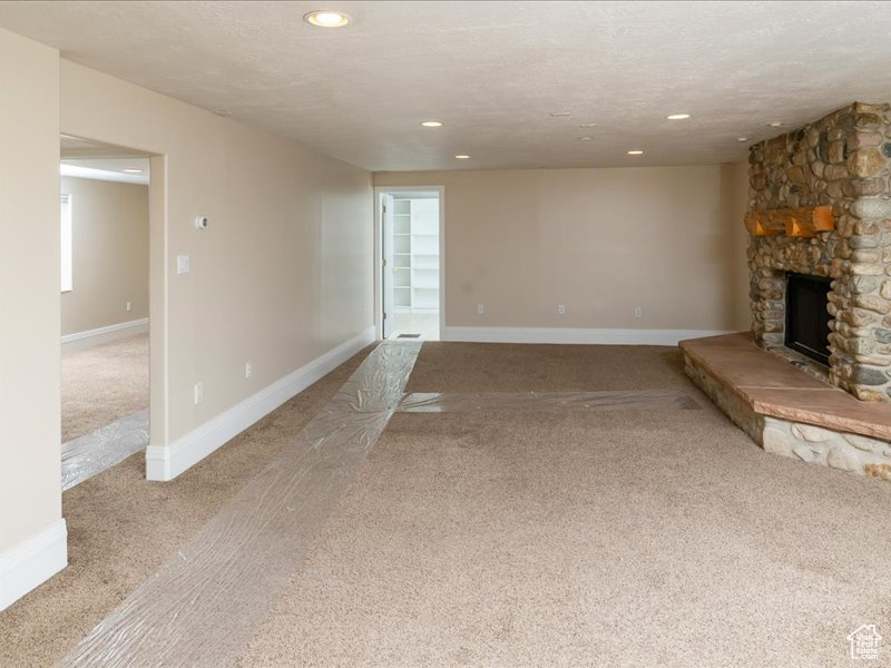 Unfurnished living room featuring a fireplace, light colored carpet, and a textured ceiling