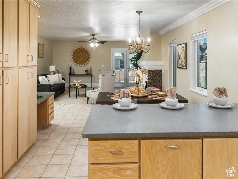 Kitchen featuring light brown cabinetry, a textured ceiling, light tile patterned floors, pendant lighting, and ceiling fan with notable chandelier