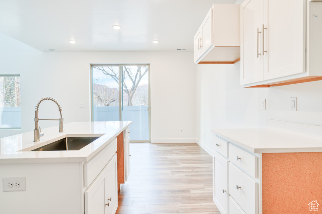 Kitchen with an island with sink, a wealth of natural light, sink, and white cabinets