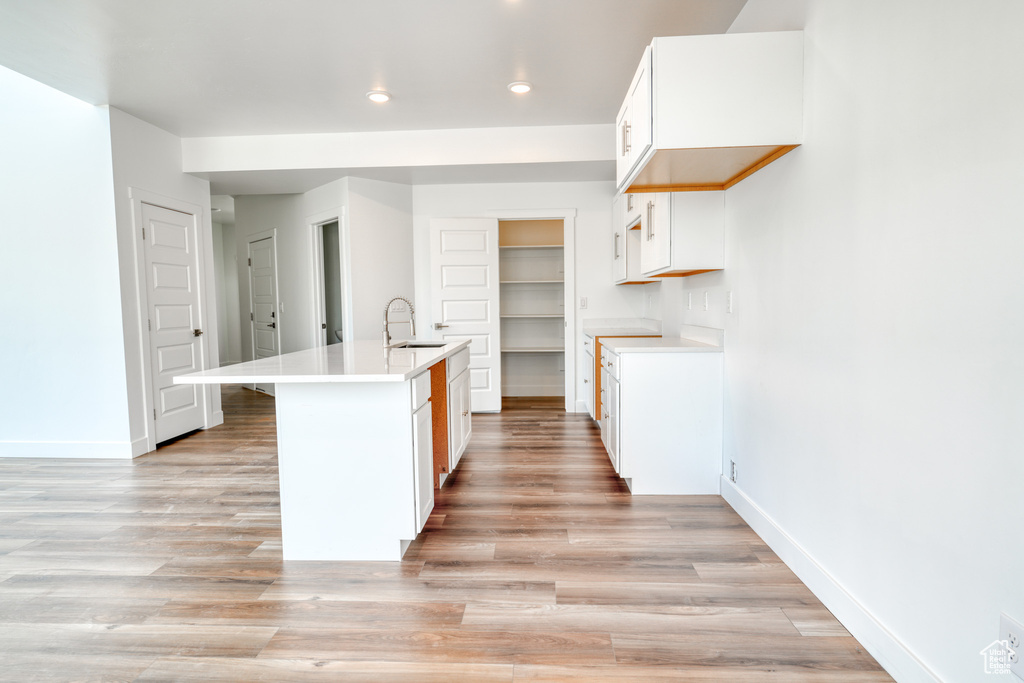 Kitchen featuring an island with sink, sink, white cabinets, and light hardwood / wood-style floors