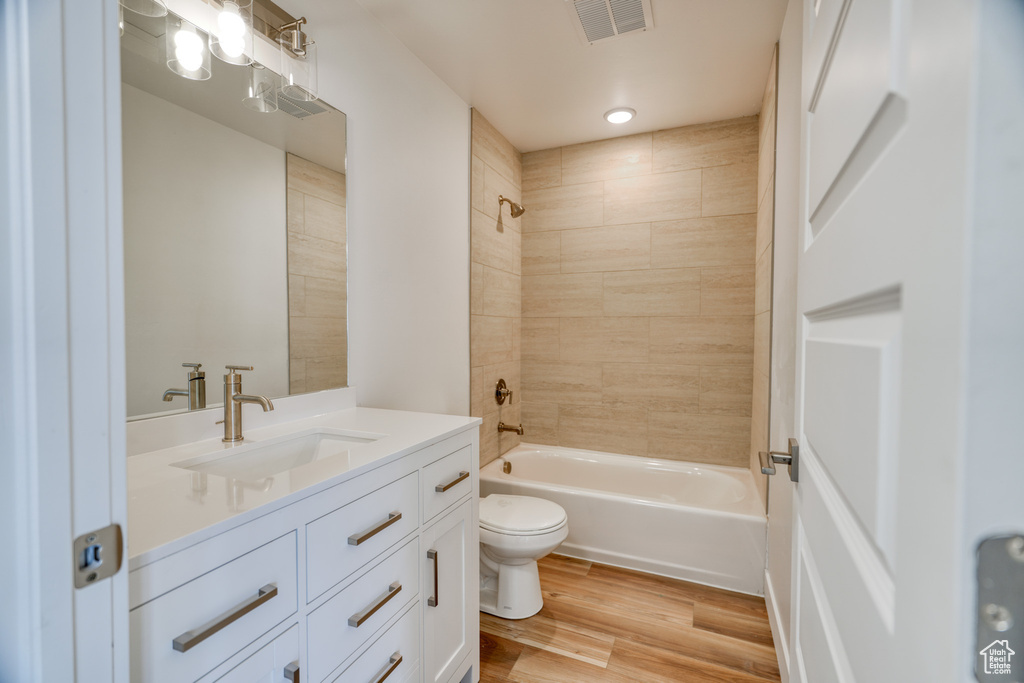 Full bathroom featuring vanity, hardwood / wood-style floors, tiled shower / bath combo, and toilet