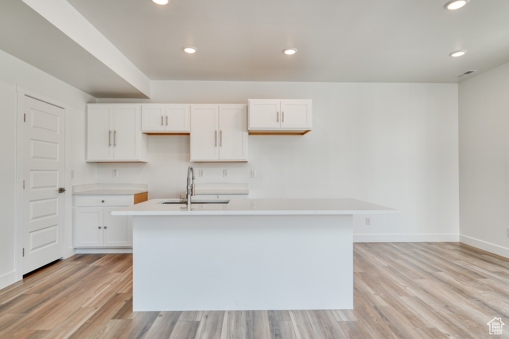 Kitchen featuring white cabinetry, sink, a kitchen island with sink, and light wood-type flooring