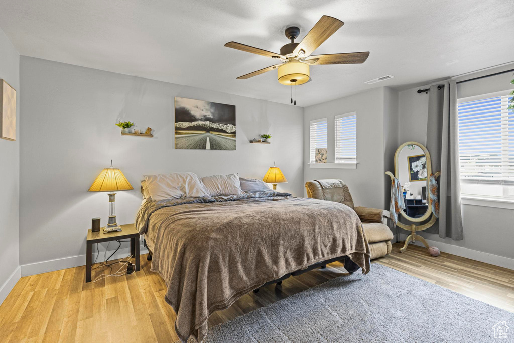 Bedroom featuring ceiling fan, multiple windows, and light wood-type flooring