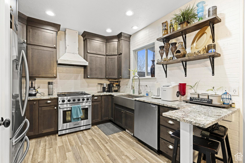 Kitchen with sink, custom exhaust hood, light wood-type flooring, appliances with stainless steel finishes, and light stone countertops