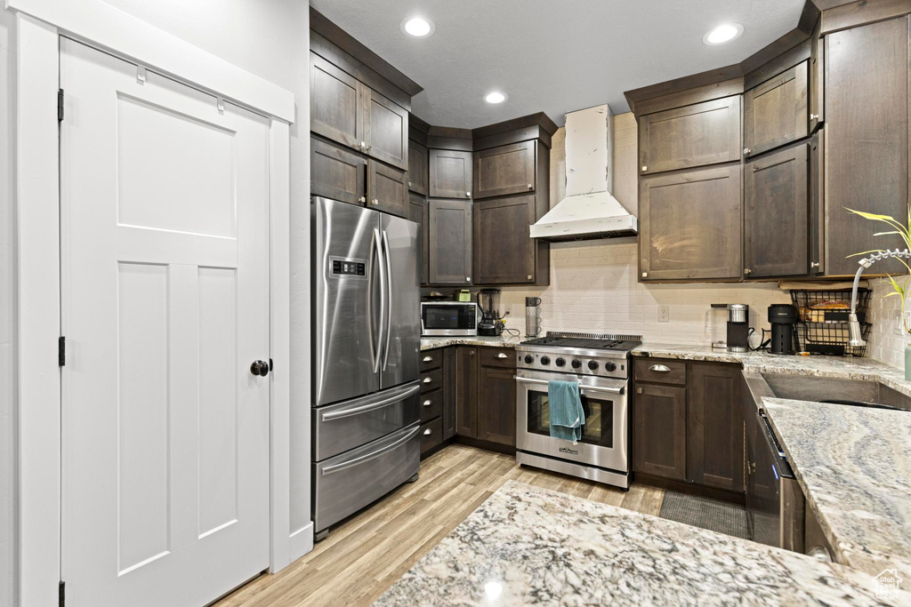Kitchen featuring appliances with stainless steel finishes, tasteful backsplash, custom exhaust hood, light hardwood / wood-style floors, and light stone countertops