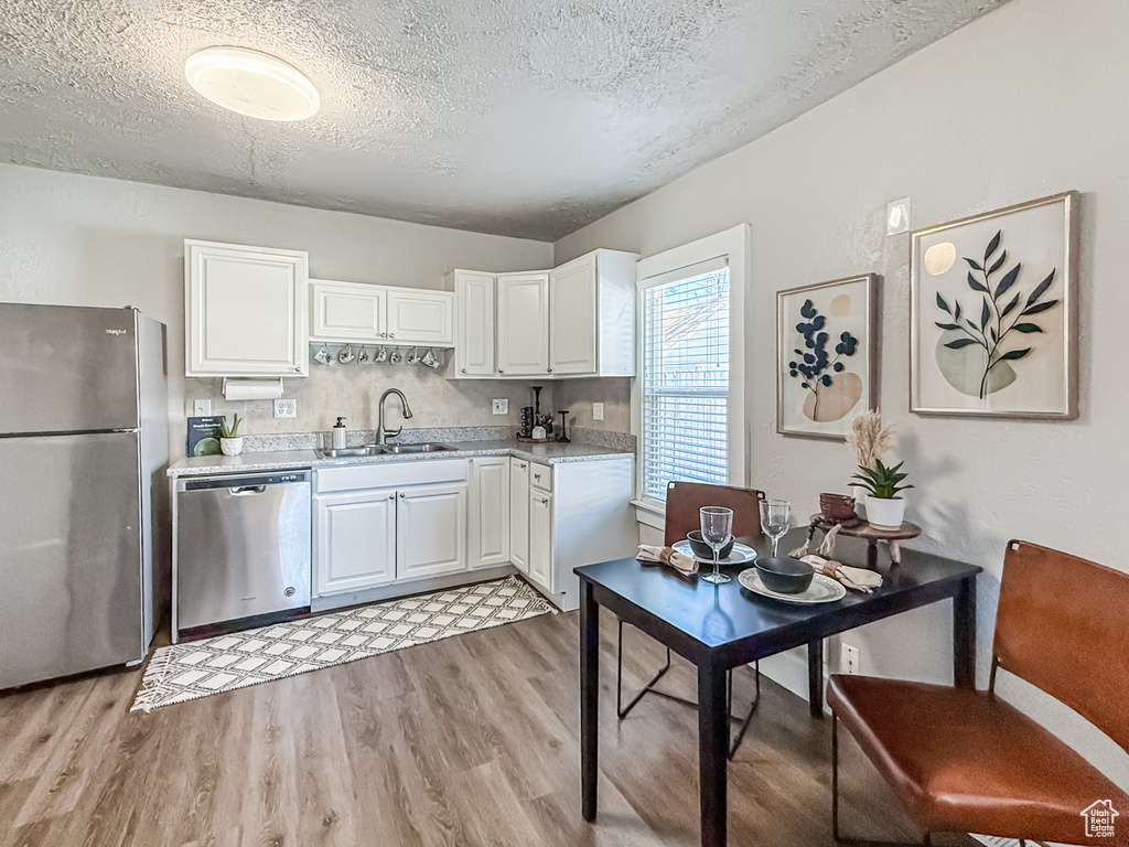 Kitchen featuring light countertops, a sink, light wood finished floors, white cabinetry, and stainless steel appliances