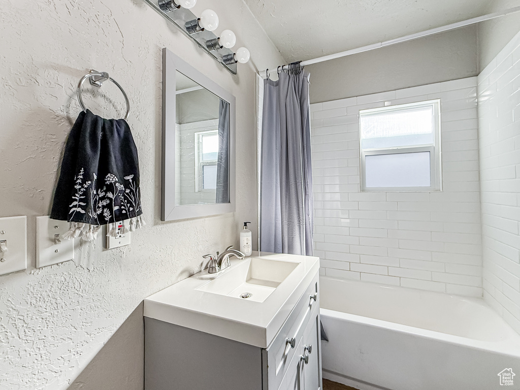 Bathroom featuring a textured wall, shower / bath combo with shower curtain, and vanity