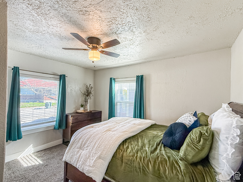 Carpeted bedroom with a textured wall, a textured ceiling, baseboards, and ceiling fan
