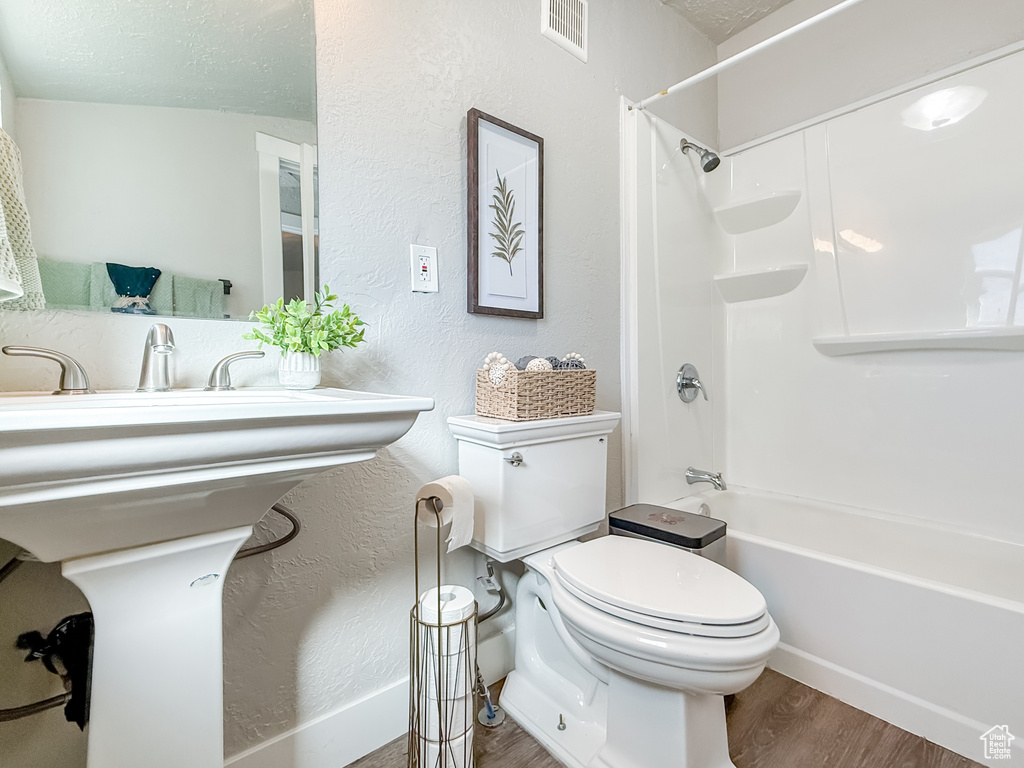 Full bath with a textured ceiling, visible vents, washtub / shower combination, toilet, and wood finished floors
