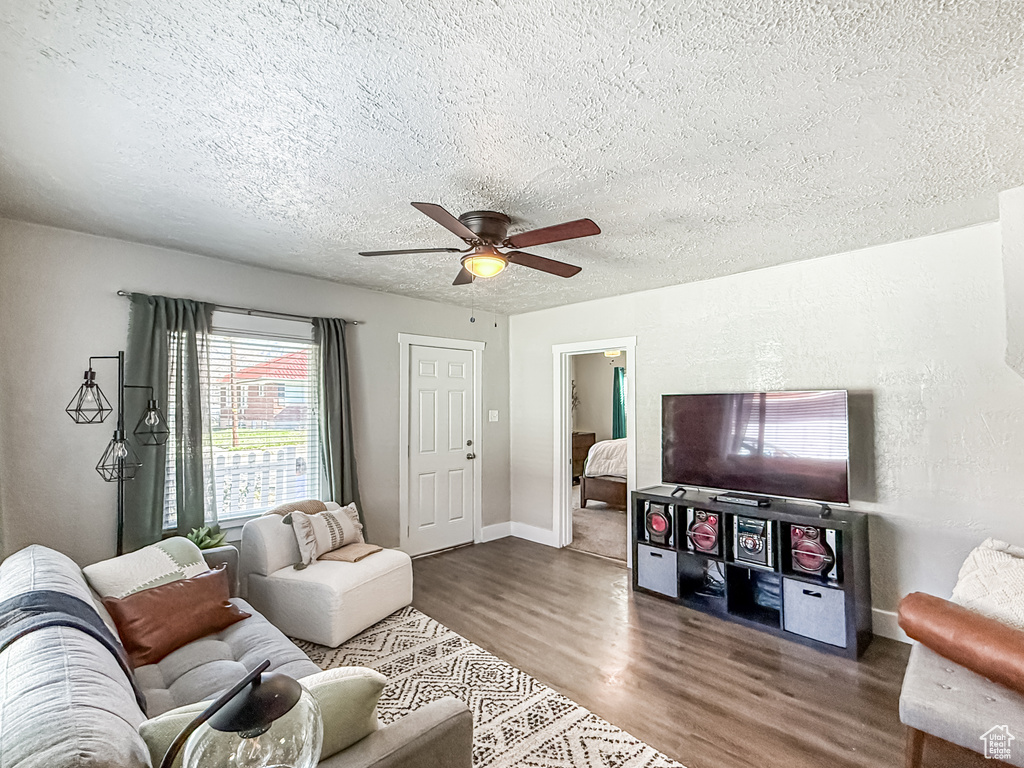 Living room with baseboards, a textured ceiling, wood finished floors, and a ceiling fan