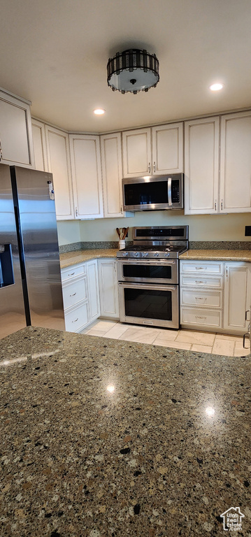 Kitchen with stainless steel appliances, dark stone countertops, and white cabinets