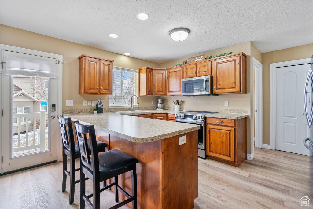 Kitchen featuring appliances with stainless steel finishes, a kitchen breakfast bar, light hardwood / wood-style floors, kitchen peninsula, and a textured ceiling