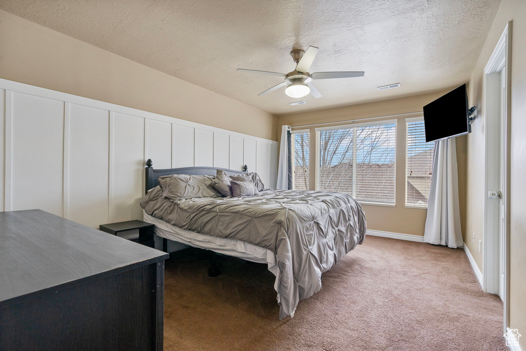 Carpeted bedroom with ceiling fan and a textured ceiling