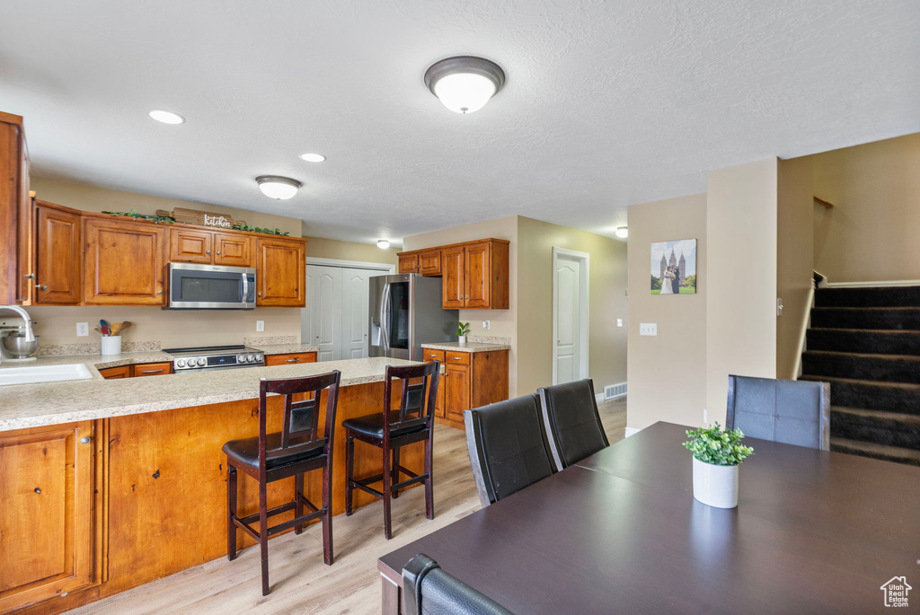 Kitchen with appliances with stainless steel finishes, sink, a kitchen breakfast bar, kitchen peninsula, and light hardwood / wood-style flooring