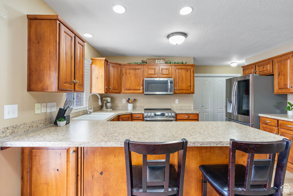 Kitchen with sink, appliances with stainless steel finishes, a textured ceiling, a kitchen bar, and kitchen peninsula