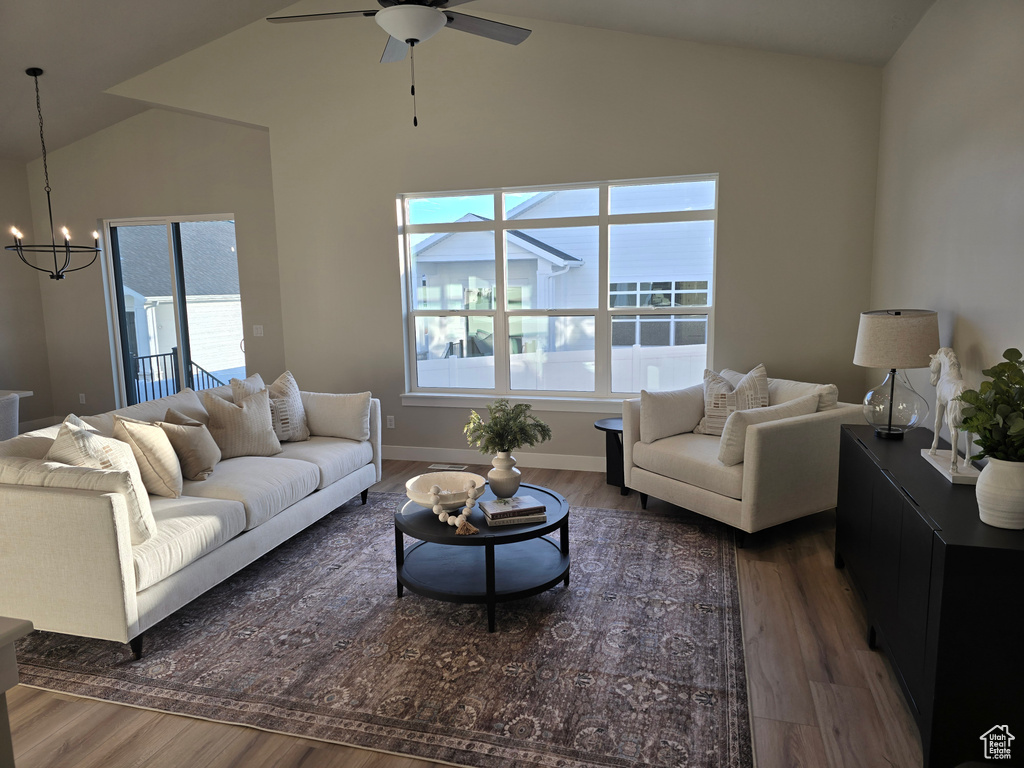 Living room with lofted ceiling, ceiling fan with notable chandelier, and dark hardwood / wood-style floors