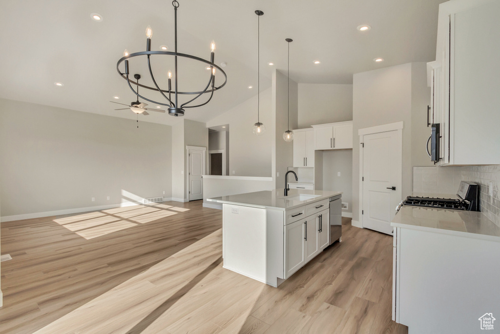 Kitchen with white cabinetry, appliances with stainless steel finishes, a kitchen island with sink, and hanging light fixtures