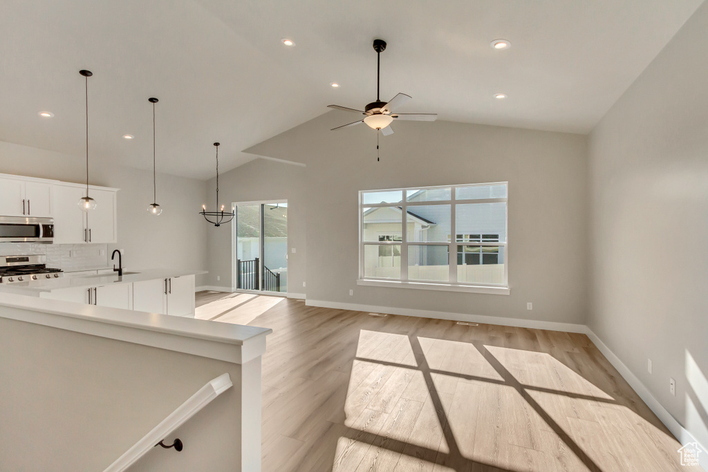 Kitchen featuring white cabinetry, tasteful backsplash, vaulted ceiling, light hardwood / wood-style flooring, and appliances with stainless steel finishes
