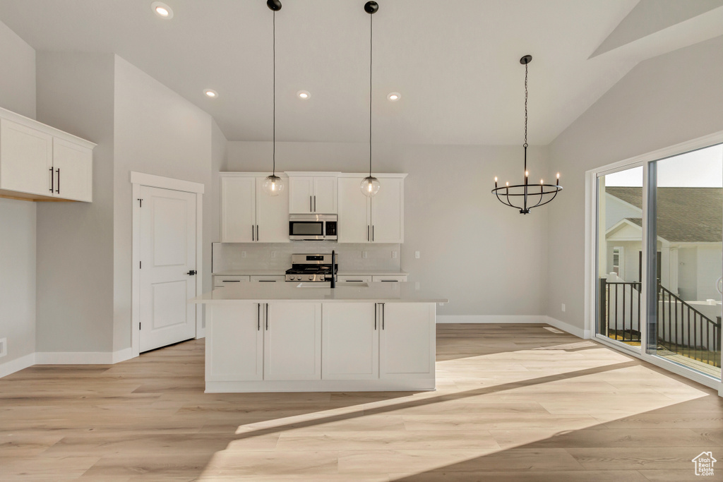 Kitchen featuring a kitchen island with sink, hanging light fixtures, white cabinets, and appliances with stainless steel finishes