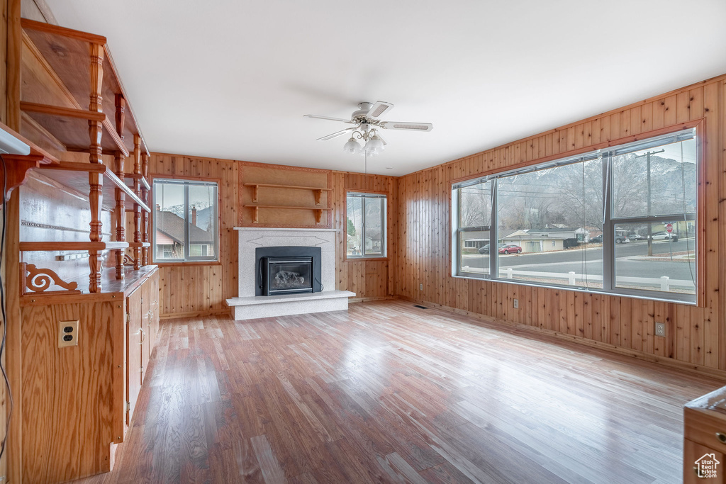 Unfurnished living room with wooden walls, ceiling fan, and light hardwood / wood-style flooring